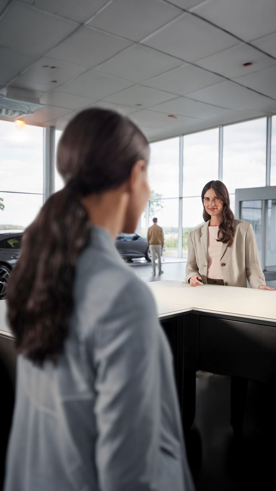 Brünette Frau steht im Autohaus am Empfang und lässt sich vone einer anderen Frau beraten