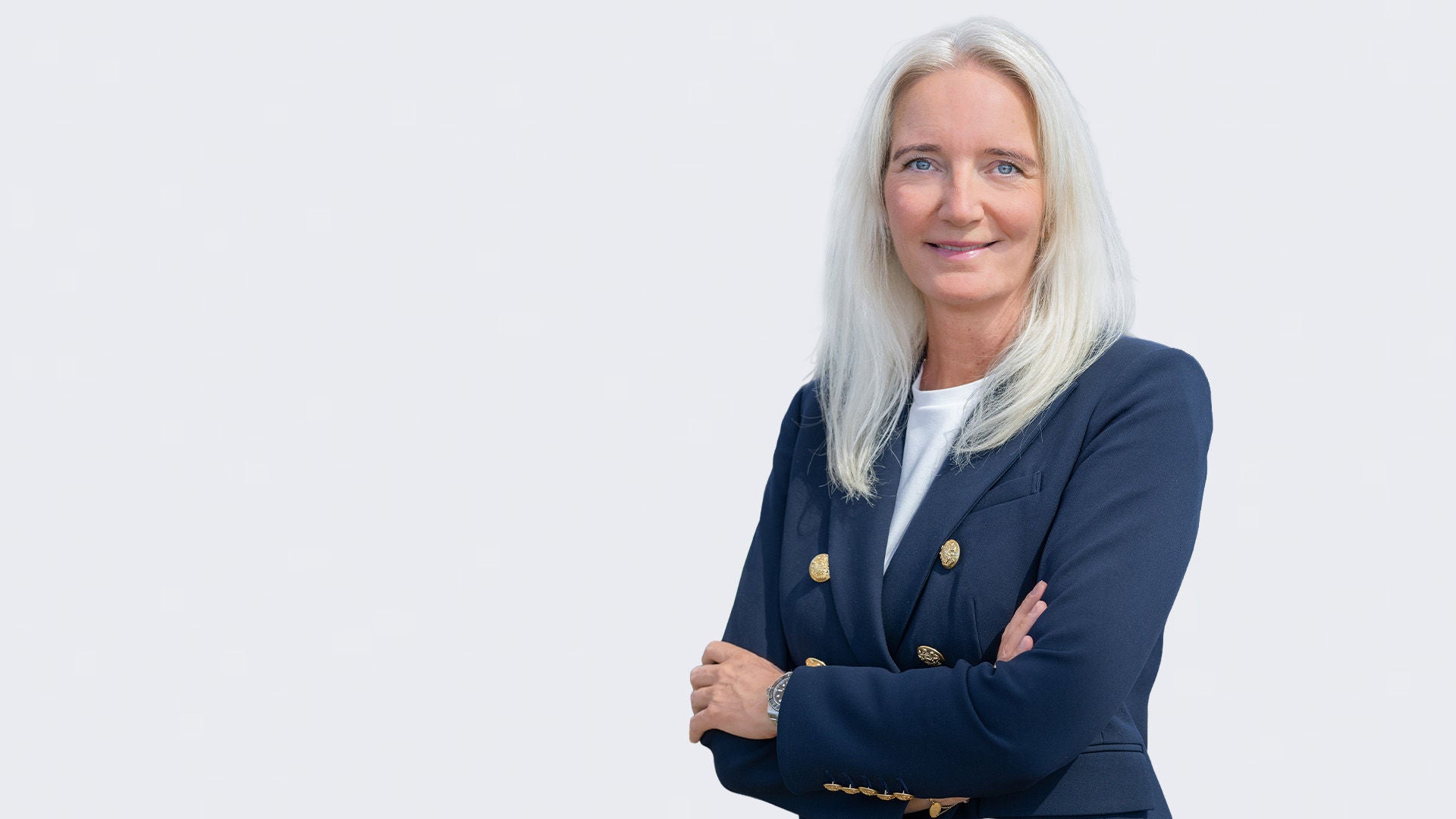 Britt Gerdes: Porträt einer lächelnden Frau im Businessoutfit vor grauem Hintergrund.