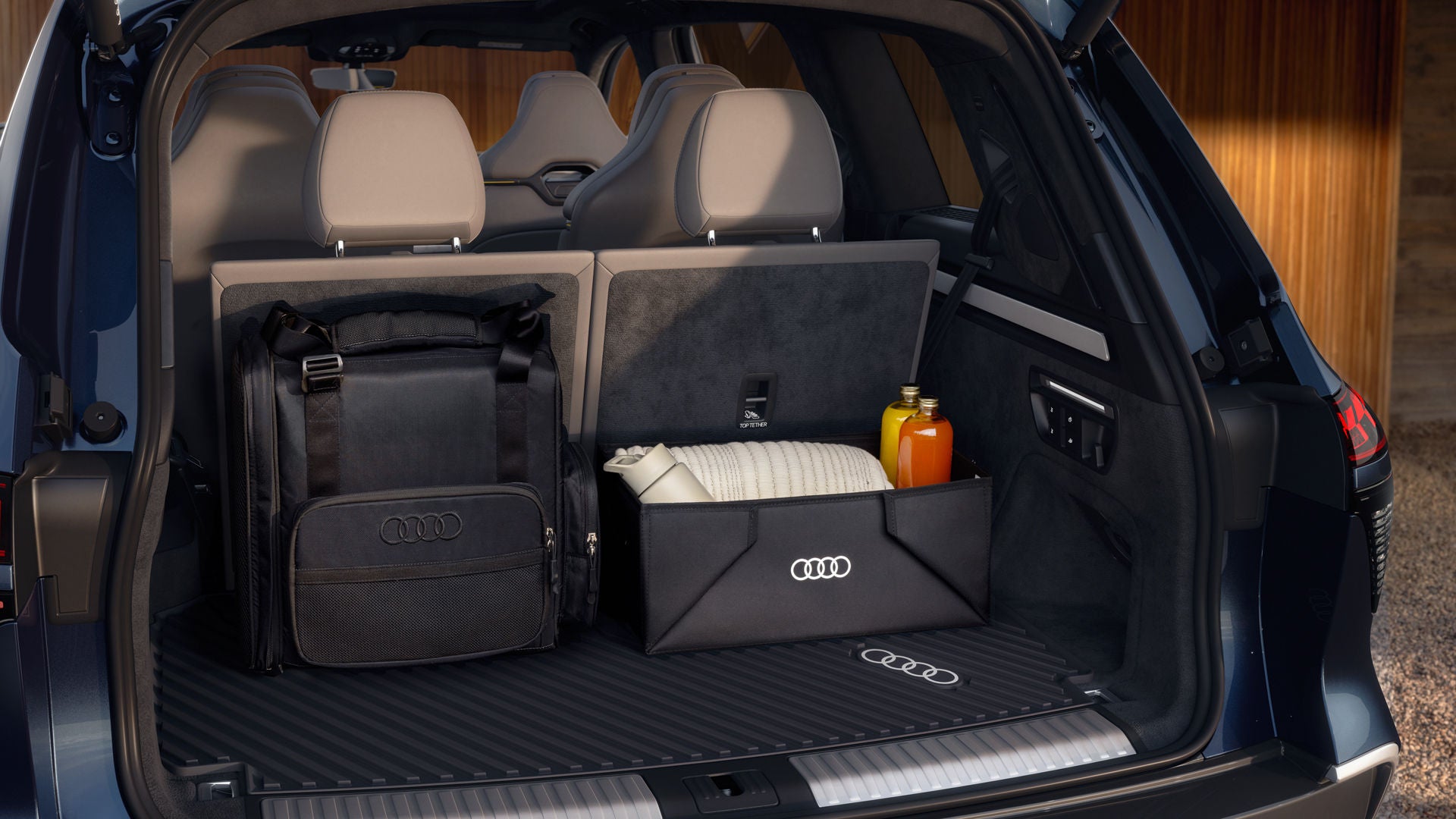 Nahaufnahme des geöffneten Kofferraums des Audi Q9 SUV. Im Inneren befinden sich die Gepäckraumschale von Audi Original Zubehör, ein Rucksack und eine faltbare Kofferraumbox.