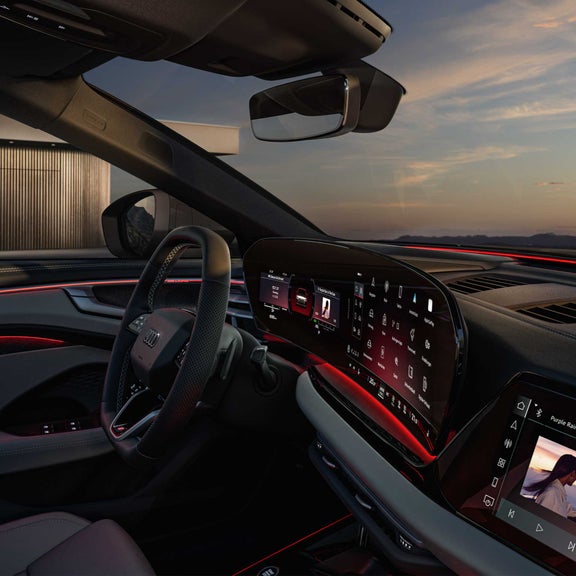 Modernes Audi-Cockpit bei Sonnenuntergang mit großem Touchdisplay, Ambientebeleuchtung in Rot und digitalem Instrumentenfeld.