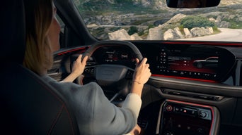 Frau am Steuer eines Audi mit digitalem Cockpit und roter Ambientebeleuchtung, Bergstraße im Hintergrund.