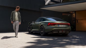 Grüner Audi RS e-tron GT performance lädt an einer Wallbox vor einem modernen Haus, ein Mann geht am Fahrzeug vorbei.