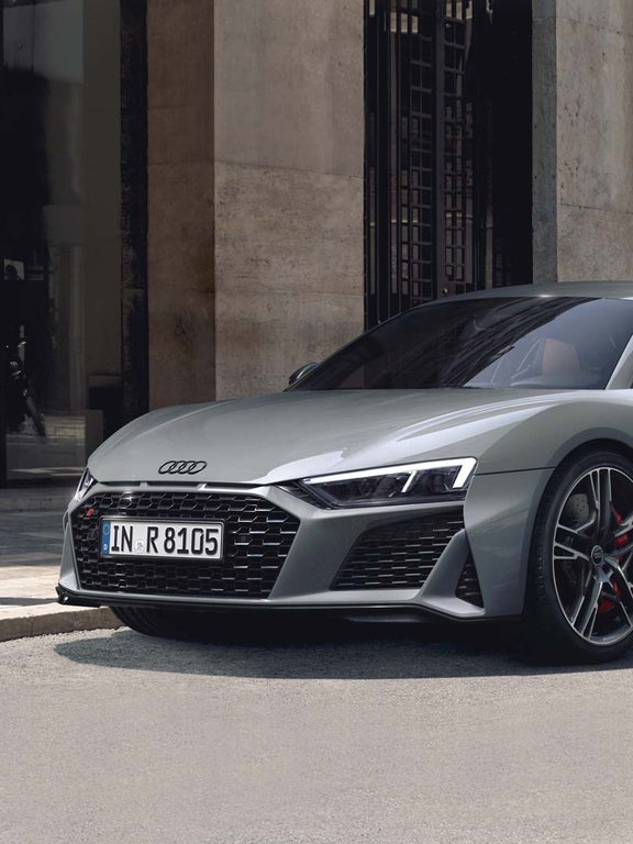 Side front view of the R8 Coupé V10 performance quattro in grey with black sideblades in front of a house