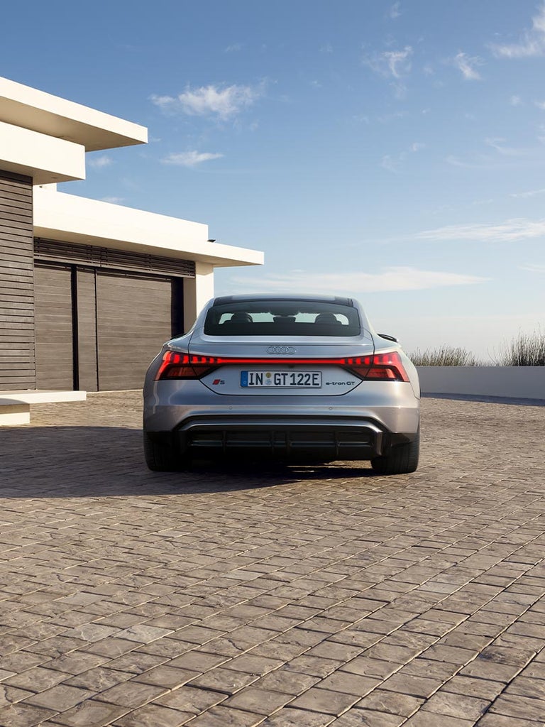Die Heckansicht des Audi S e-tron GT auf einer gepflasterten Einfahrt. Die durchgehende LED-Lichtleiste und der sportliche Diffusor betonen das dynamische Design.