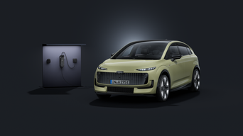 L'Audi A2 e-tron, vue de face sous un angle, sur un fond sombre, avec une borne de recharge à gauche, derrière elle.