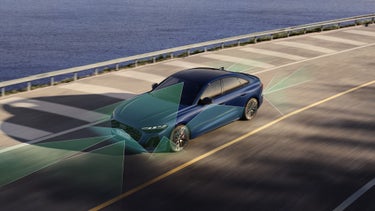 Die S5 Limousine von schräg oben, während sie auf einer Straße, am Ufer eines Gewässers entlangfährt. Vom Heck und der Front aus unterteilen grüne und blaue Vektoren die Flächen hinter und vor dem Fahrzeug.&nbsp;