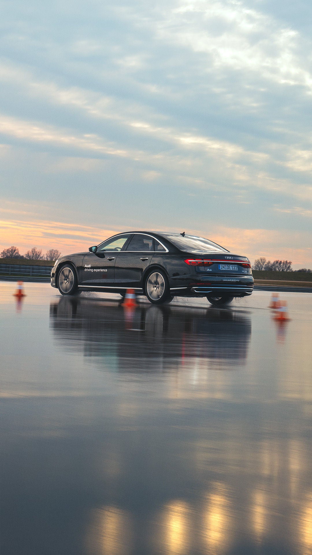 Schwarzer A8 50 TDI quattro auf nasser Strecke mit Parcour, im Hintergrund ist die Abenddämmerung.