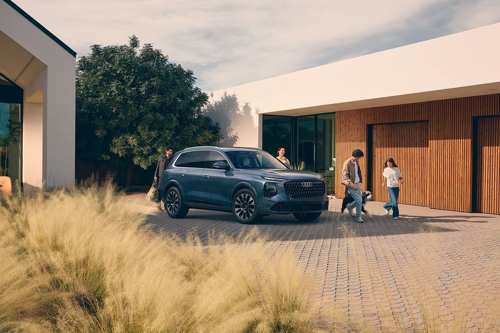 En Audi Q7 står parkerad på en garageuppfart, en familj är samlad runt bilen.