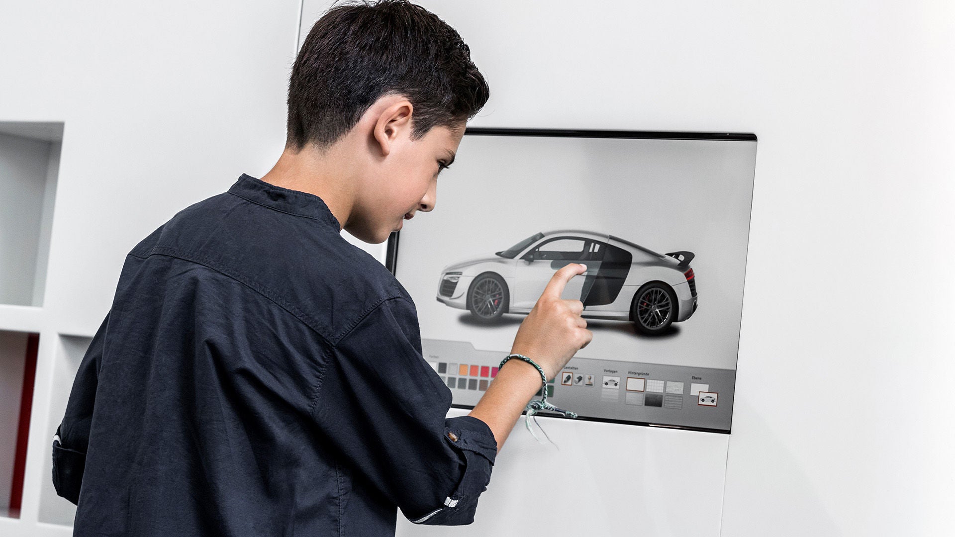 Boy operates a touchscreen with a car configurator on which a silver sports car is displayed.