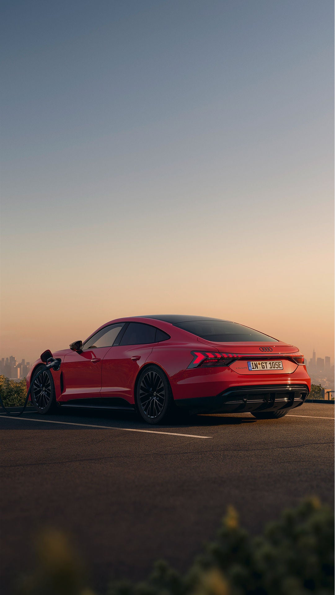 A couple standing next to a red Audi e-tron GT that's plugged into an EV charger