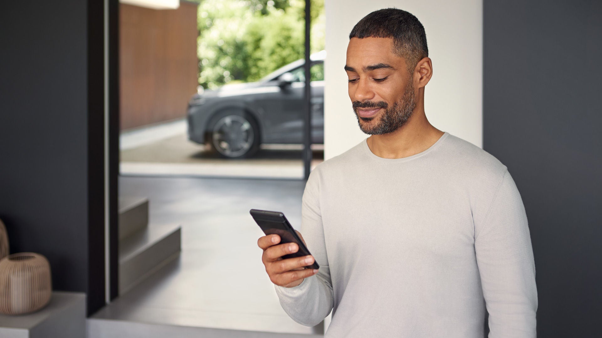 Ein Mann schaut runter auf sein Handy. Im Hintergrund ist unscharf ein graues Audi Modell zu sehen.