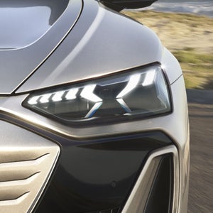 Eine frontale Nahaufnahme des Audi S e-tron GT auf einer Straße an der Küste. Die imposante Lichtsignatur der Scheinwerfer und das sportliche Design stehen im Fokus.