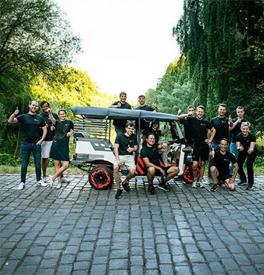 Gruppe posiert mit vollen orangenen Säcken um eine E-Rikscha herum