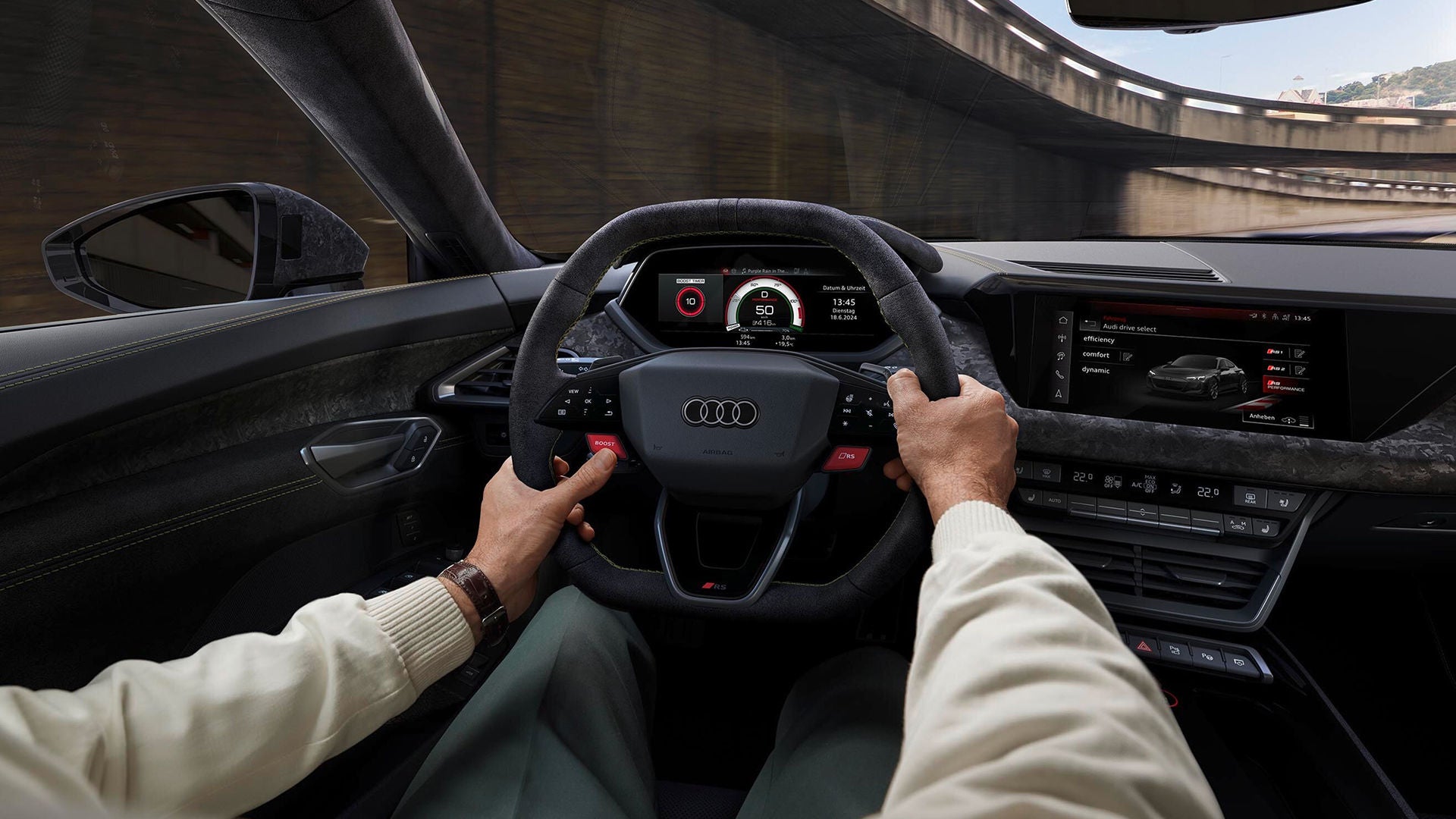 Close-up of a person driving an Audi, hands on the steering wheel. The digital dashboard displays speed, surrounded by a modern interior design.