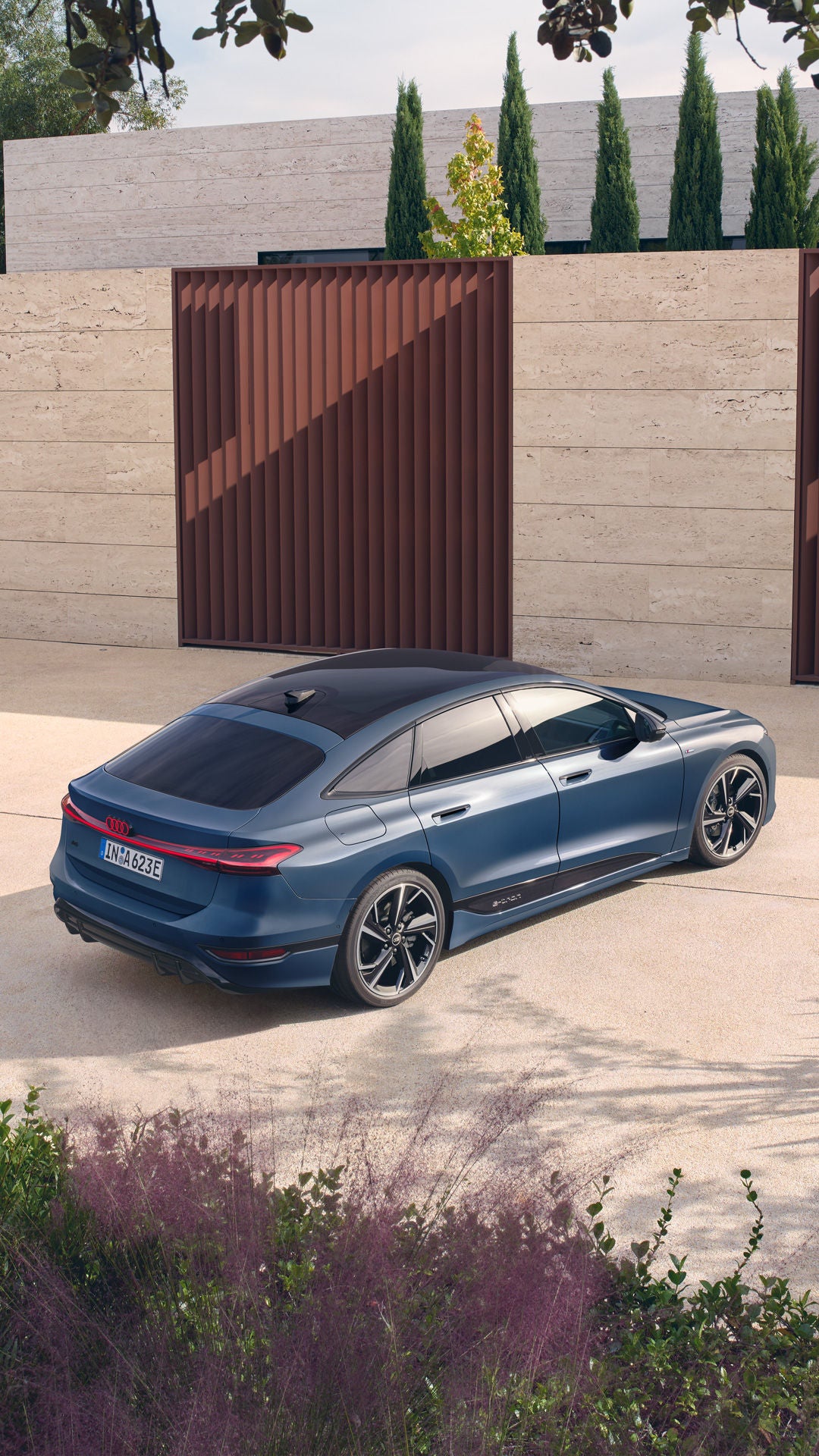 Ein blauer A6 Sportback e-tron geparkt in einem modernen Innenhof mit hellen Steinwänden und vertikalen Holzlamellen, umgeben von dezenter Bepflanzung.