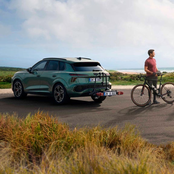El Q3 SUV con portabicicletas se encuentra frente a un paisaje costero, junto a él un joven con una bicicleta de grava.