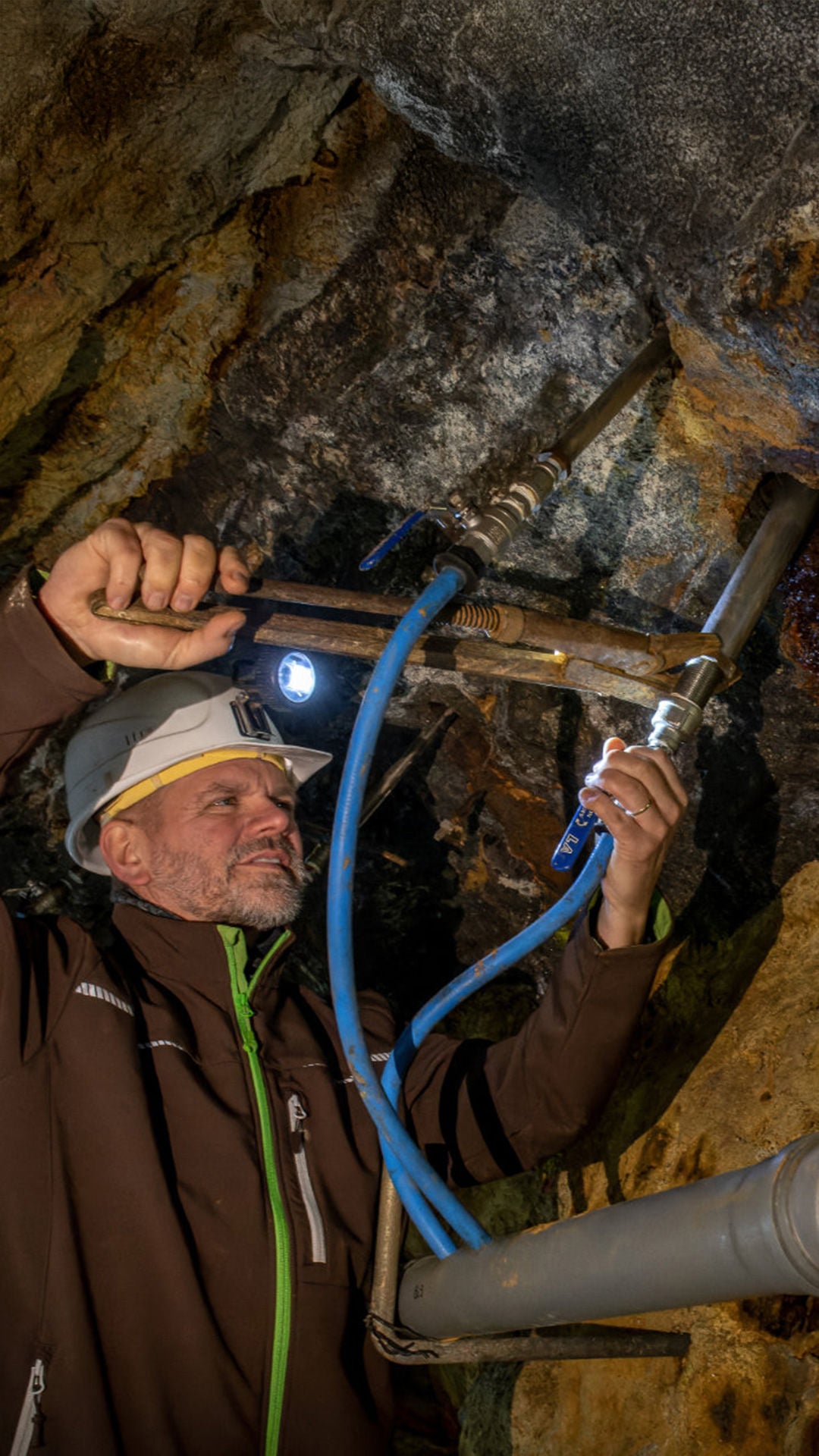 Mann mit Sicherheitkleidung bohrt in einem Bergstollen ein Loch in die Felswand.