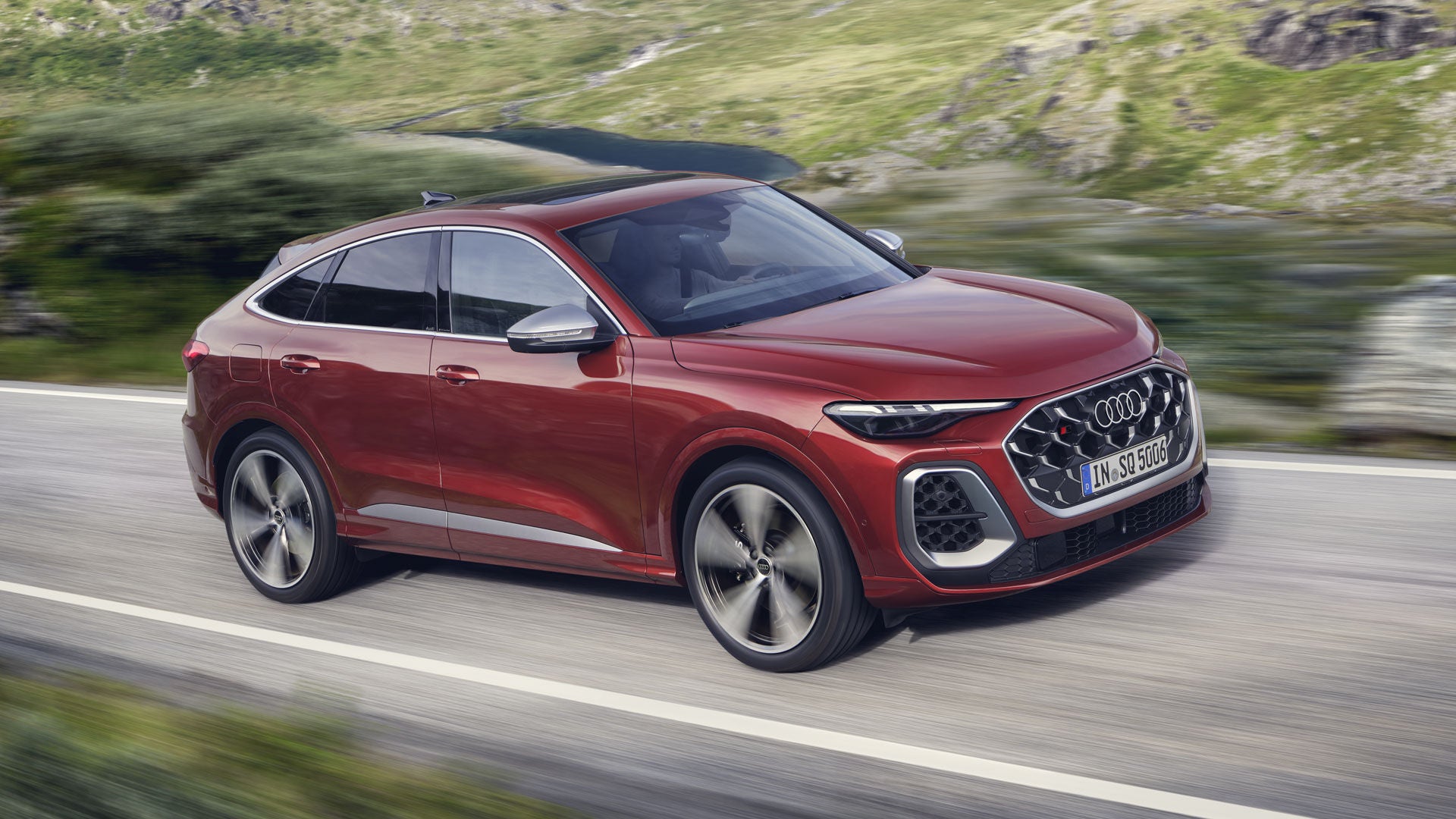 Der rote SQ5 Sportback fährt über eine Straße in den Bergen. Ein junger Mann sitzt am Steuer.