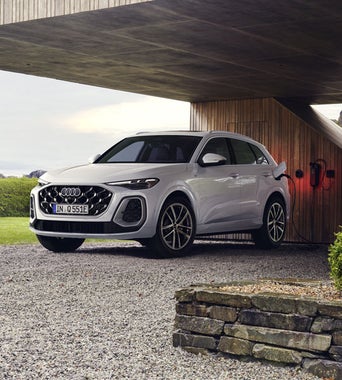 The all new Q5 SUV e-hybrid in front of a modern rural home, charging at a charging station for residential buildings