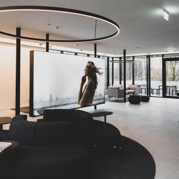 Moderne, helle Audi Lounge mit Sitzmöbeln, großem Bildschirm und Panoramafenstern, ohne Personen im Raum.