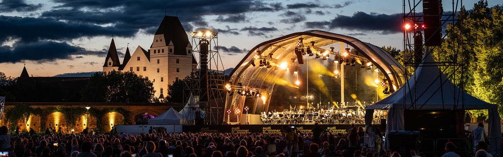Audi Sommerkonzerte Open-Air-Bühne bei Dämmerung mit Publikum vor historischem Schloss in Ingolstadt.