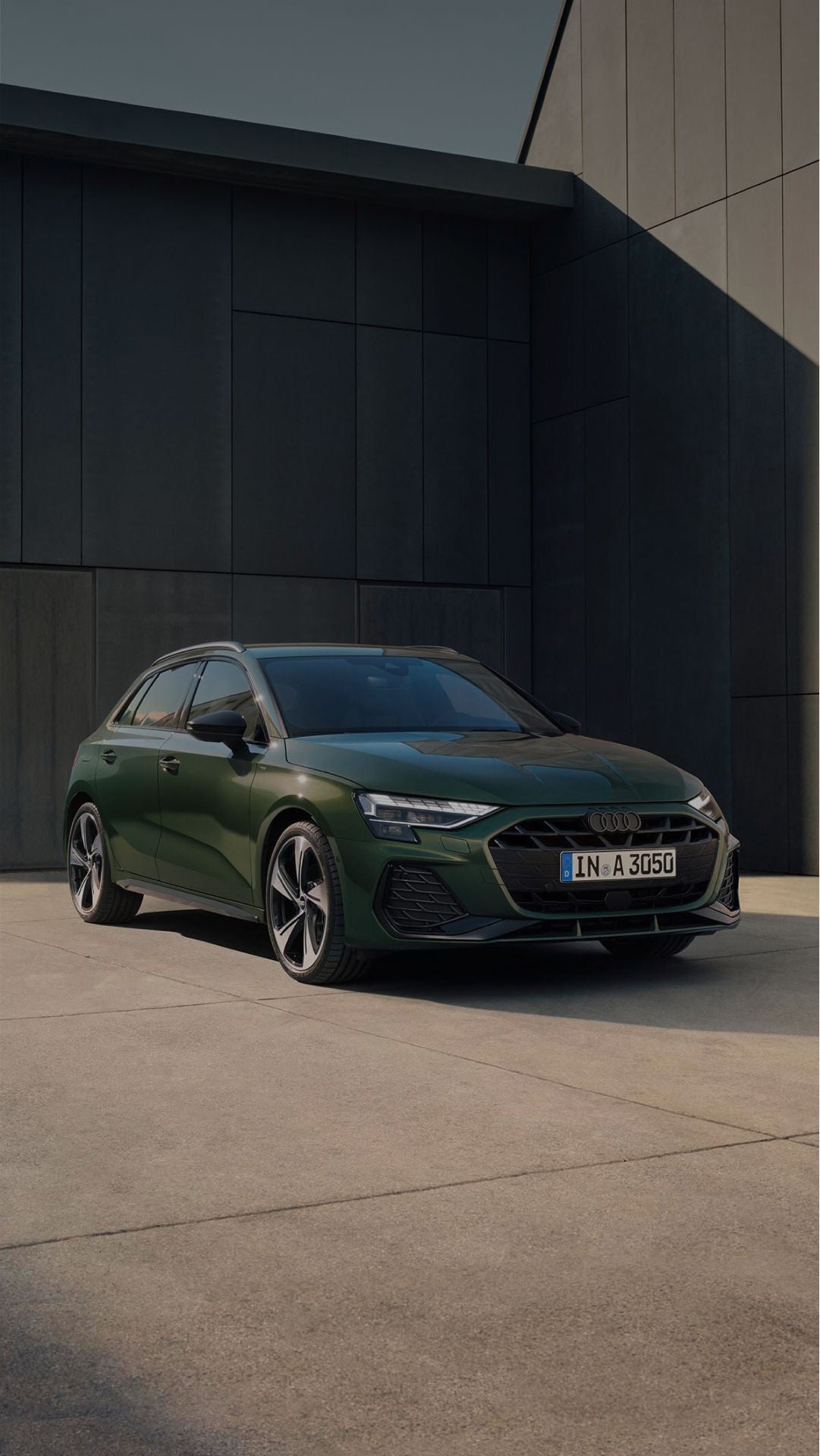 A parked green Audi car in front of a modern building
