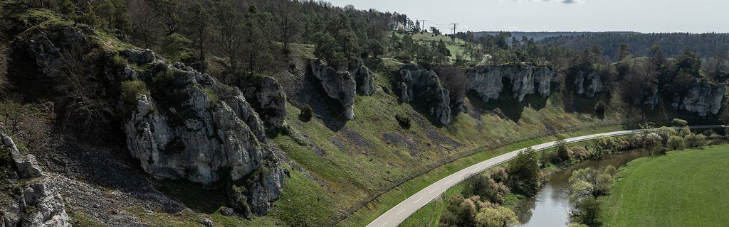 A landscape with rocks, a winding road, and a river flowing between green hillsides.