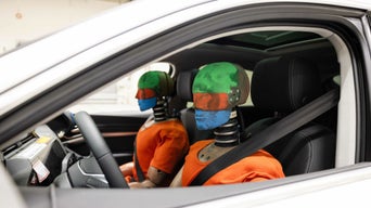Auf dem Fahrer- und Beifahrersitz eines Audi sitzen zwei Dummys für einen Crash-Test