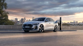 A young woman stands in front of a charging station, about to recharge a white A6 sedan e-hybrid.	