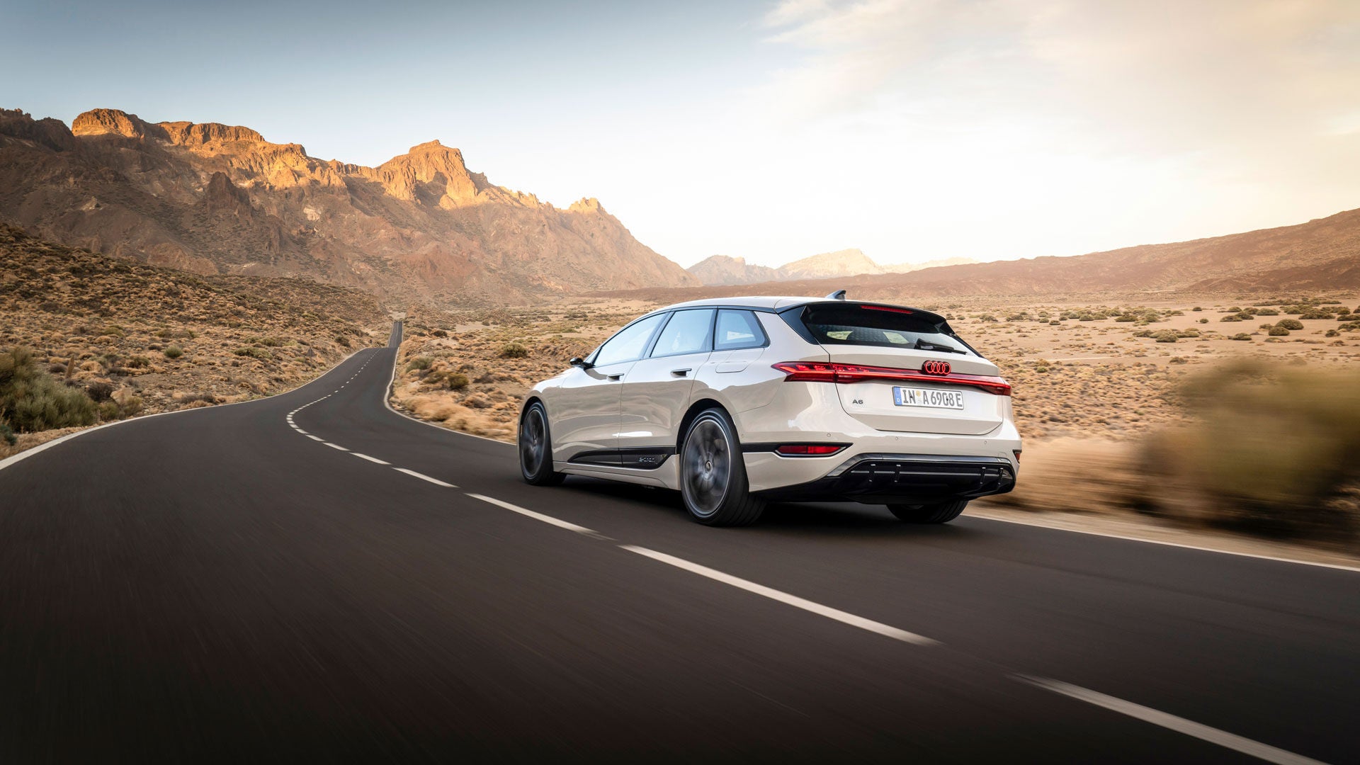 Ein Audi A6 Avant e-tron fährt über eine Wüstenstraße. Im Hintergrund eine Bergkette in der Morgensonne