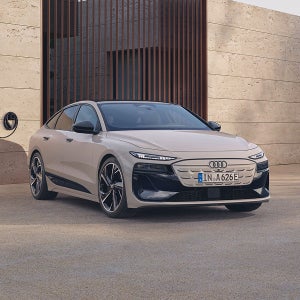 A beige Audi sedan is parked in front of a contemporary concrete building with vertical wooden slats, conveying luxury and sophistication.