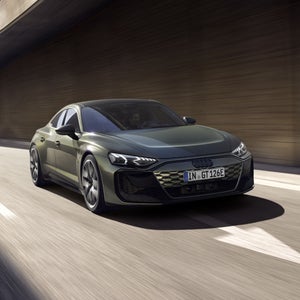 Um Audi RS e-tron GT performance verde passa por baixo de uma ponte de concreto em uma estrada de várias faixas com efeito de movimento.