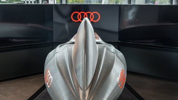 Rückansicht eines Audi racing Simulators mit silberner Rückenflosse vor leuchtenden Audi-Ringen.