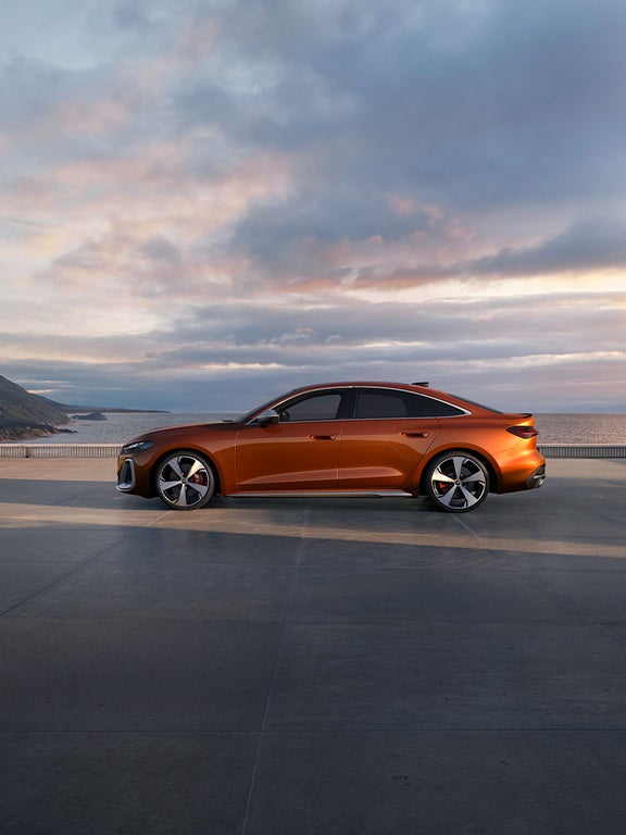 Kupferorange Audi S5 Limousine seitlich vor Küstenkulisse, eine Person geht daneben entlang.