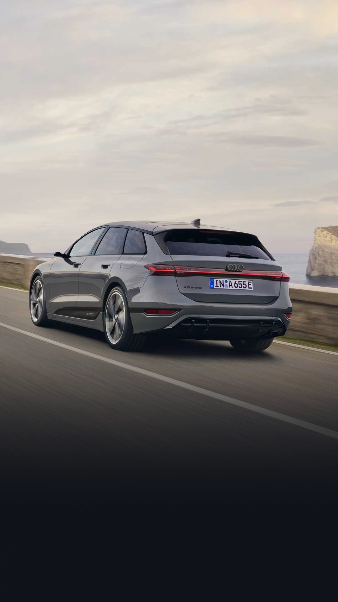 Rear view of the A6 Avant e-tron driving along a road by the sea. Rocks and mountains can be seen in the background.