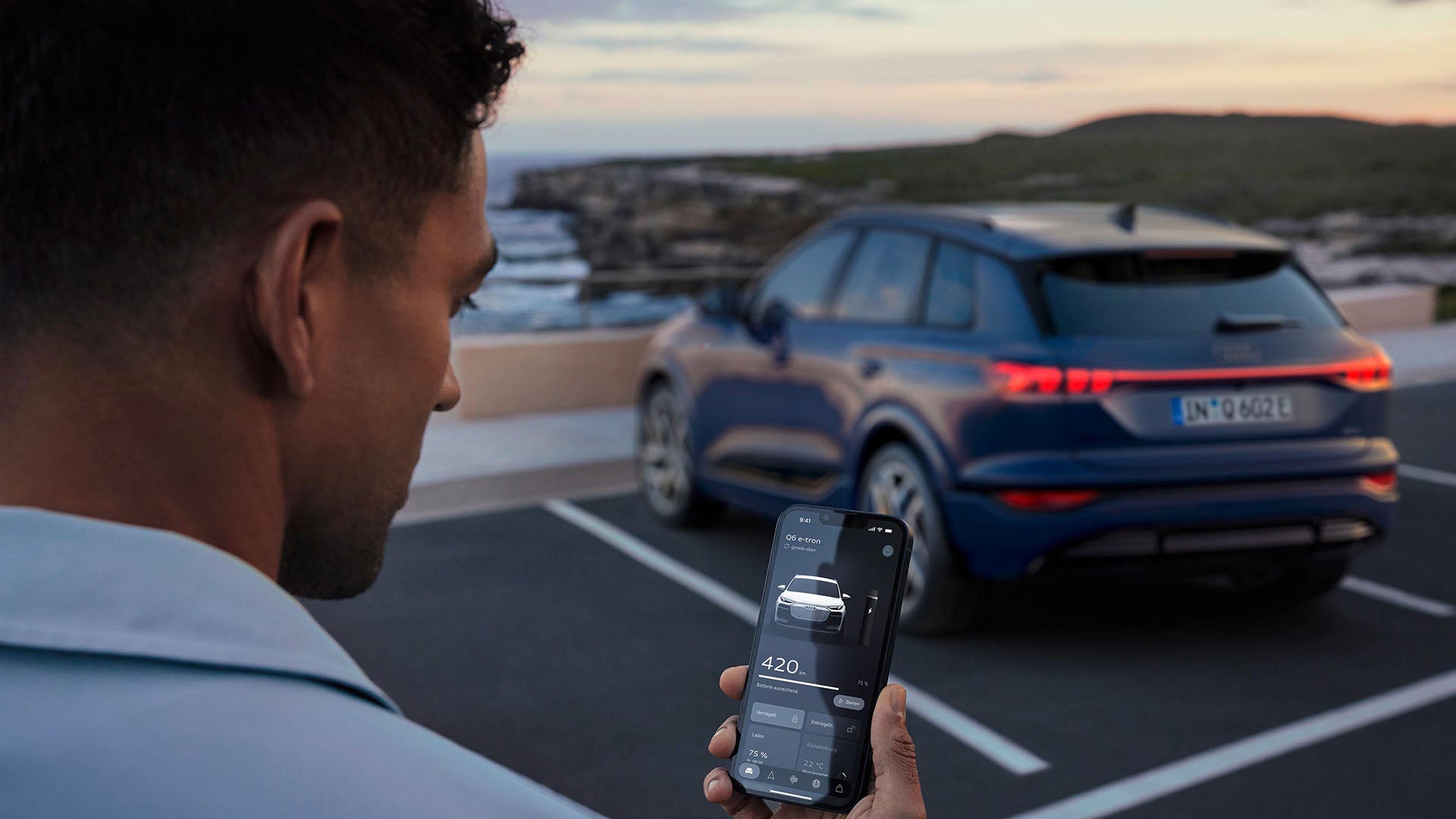Ein Mann steht neben einem blauen Audi SUV und bedient ihr Smartphone