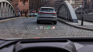 Grey Audi Q4 e-tron driving on cobblestone road; bridge arches either side; Audi's head-up display technology in centre of windshield.