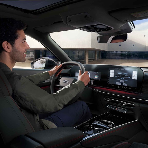 Audi Q3 Sportback interior. A man can be seen sitting in the car with his hands on the steering wheel. The panorama display showing various seat settings can also be seen.