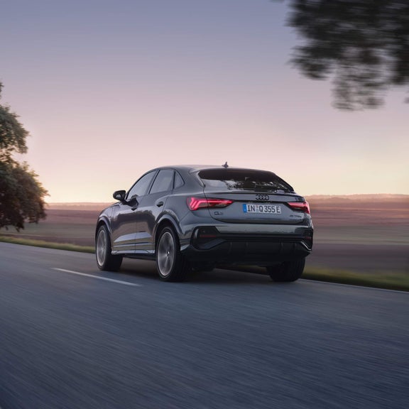 Rear view of Q3 on a rural open road with skyline of mountains in the background.