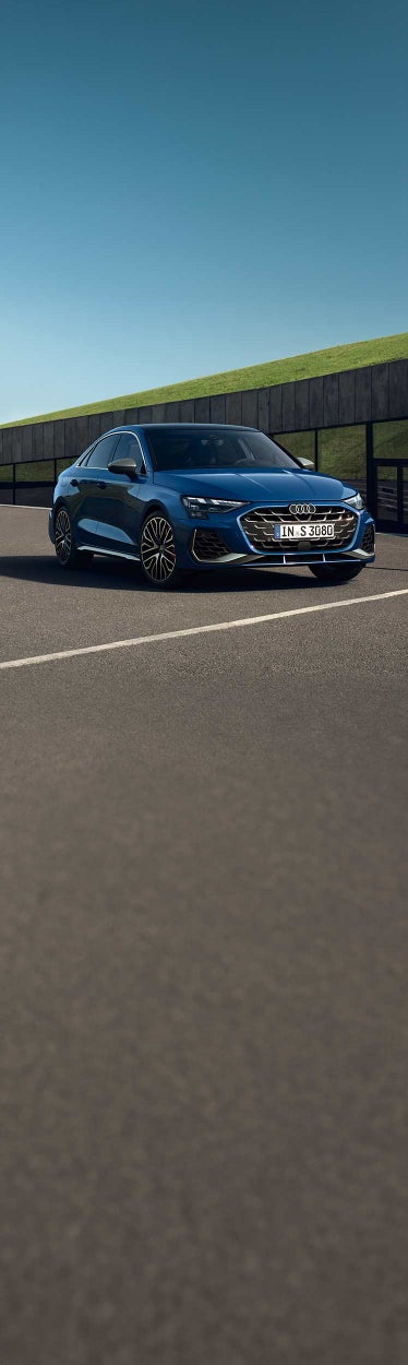 Blauer Audi S3 Limousine steht auf einem Asphaltplatz vor einem modernen Gebäude mit dunkler Glasfassade.