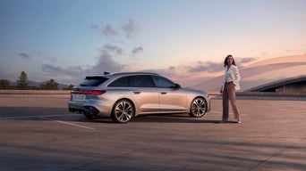 Mann zeigt Frau ein Tablet in modernem Audi-Autohaus, auf dem Tisch davor stehen zwei Gläser Wasser und ein Smartphone.