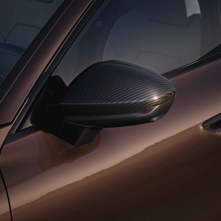 Detailaufnahme eines Außenspiegels mit schwarzem Carbongehäuse an braunem Audi A6 Avant, Sonnenlicht spiegelt auf dem Gehäuse.