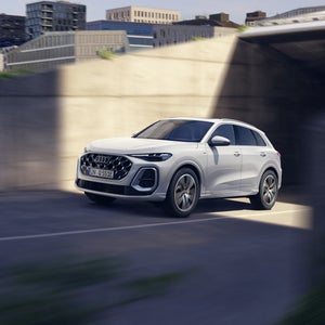 framifrånvy av en vit Q5 SUV e-hybrid som kör på en väg i en stad.