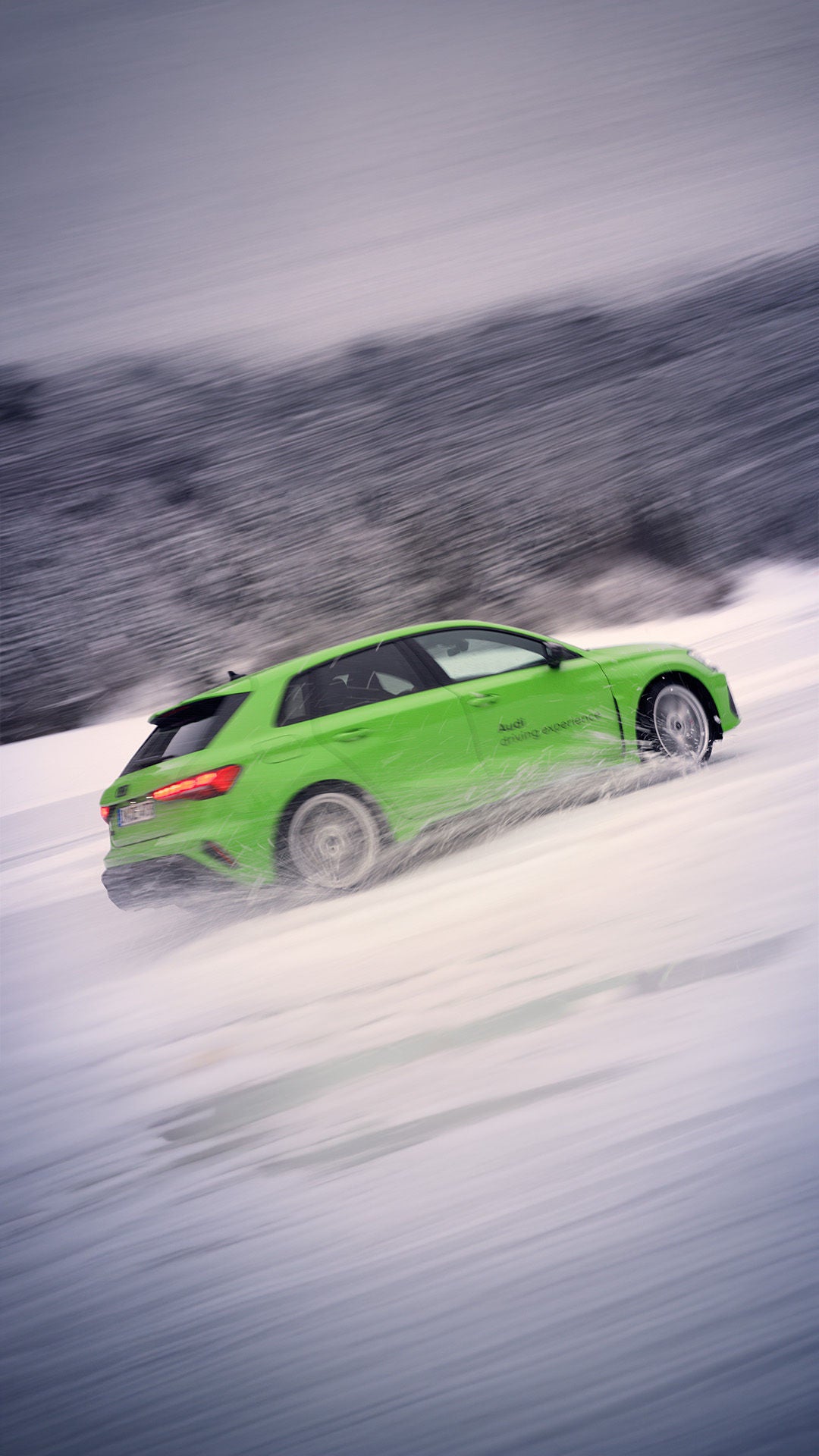 A light green Audi RS 3 Sportback sends water and snow flying as it drifts through the snow.