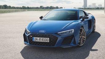 Blue Audi R8 Coupé parked in an open space with a view of a city in the background.