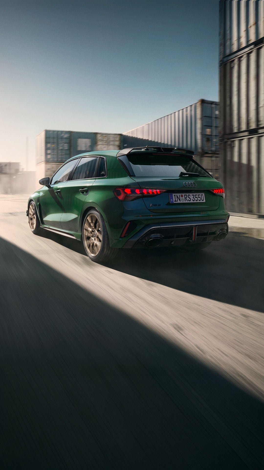 9084: Das Sondermodell RS 3 competition limited schräg von hinten fährt durch eine Straßenschlucht, gesäumt von Containern.