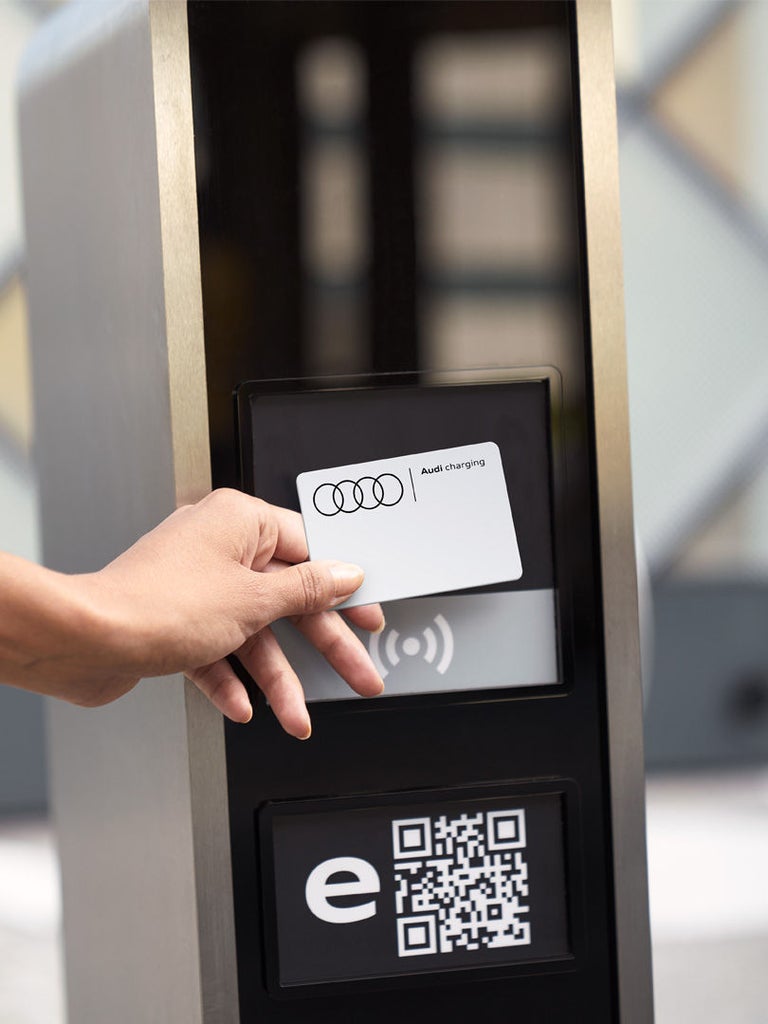 Eine Hand hält eine Audi-Charging-Karte vor ein Lesegerät an einer Ladestation.