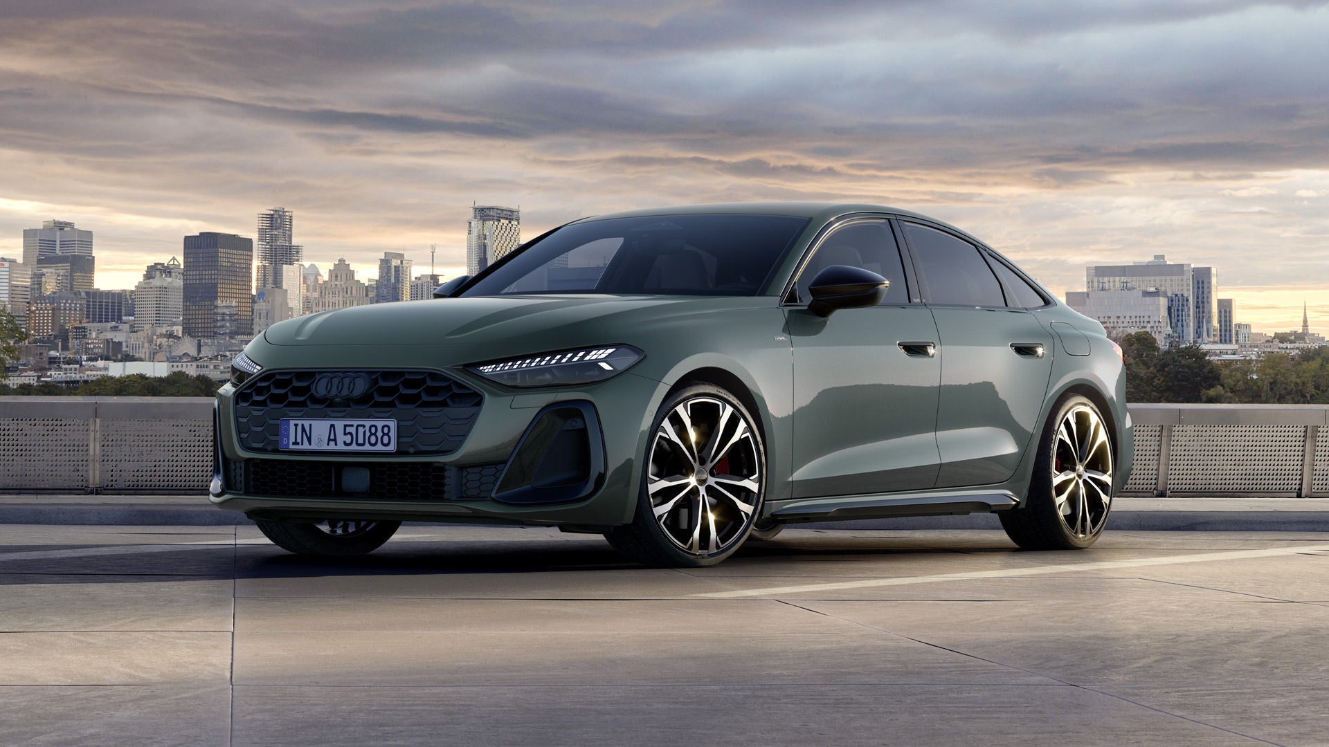 En A5 e-hybrid med kamouflagegrön metallic-lackering, sedd snett framifrån. En stadssilhuett i bakgrunden.