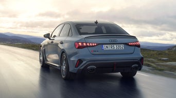 Die RS 3 Limousine von schräg hinten fährt auf einer Gebirgsstraße bei bewölktem Himmel.