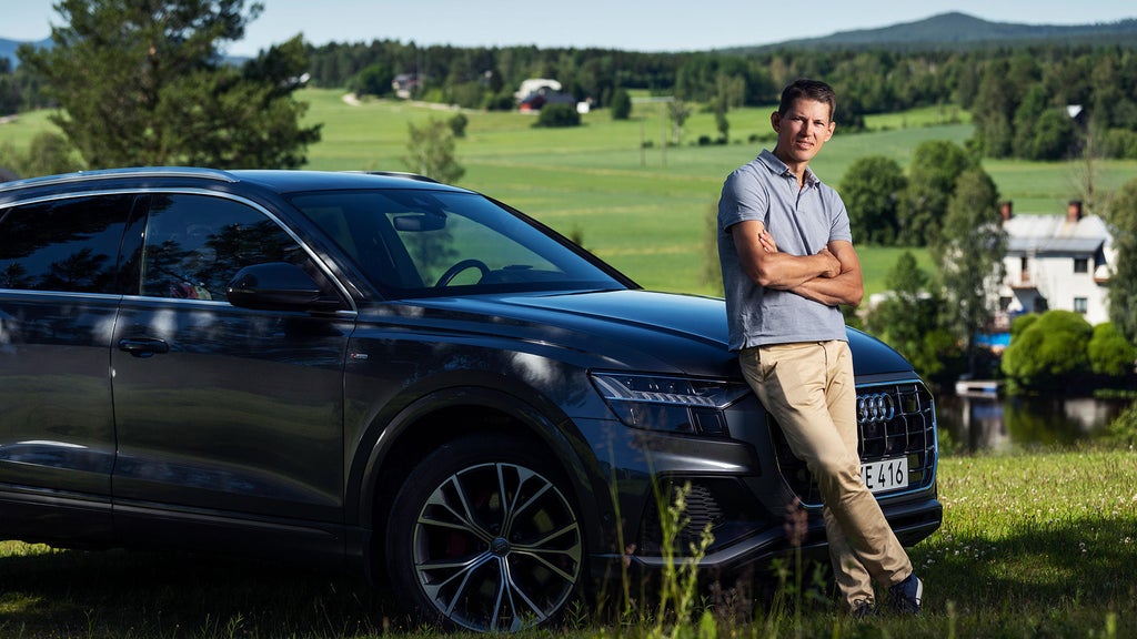  André Myhrer lutandes mot motorhuvudet på sin Audi med ängar bakom